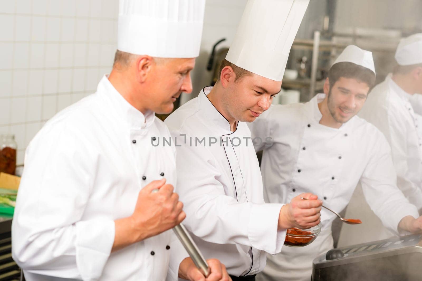 Two male cooks working in professional industrial kitchen prepare food