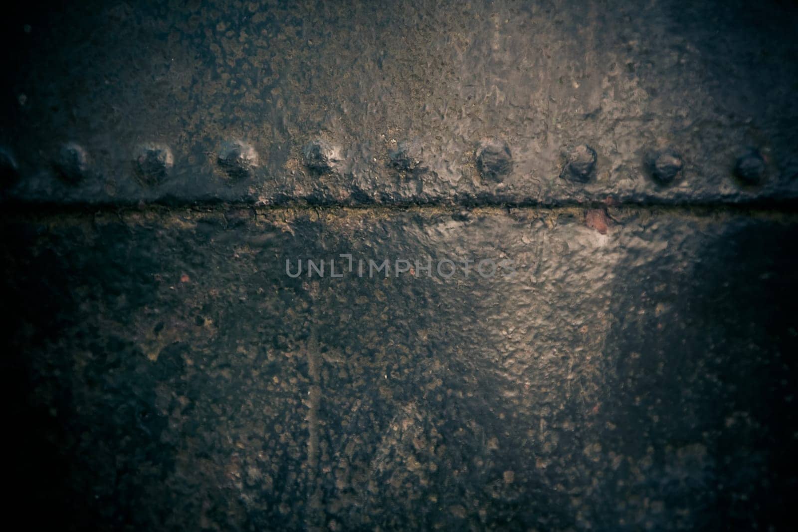 Pitted surface texture of old metal painted black with central highlight and riveted join