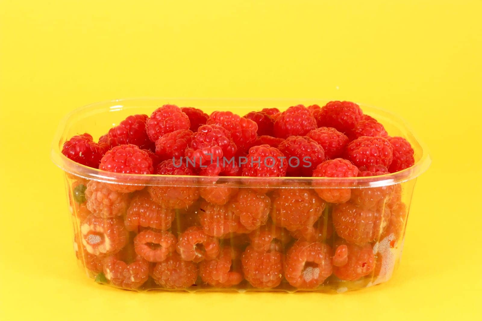 Fresh raspberries in plastic container on yelow background