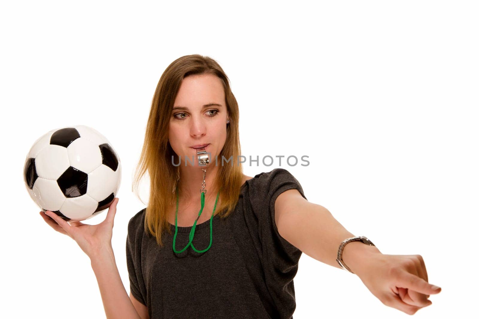 Woman with soccer ball and whistle pointing at something against white background