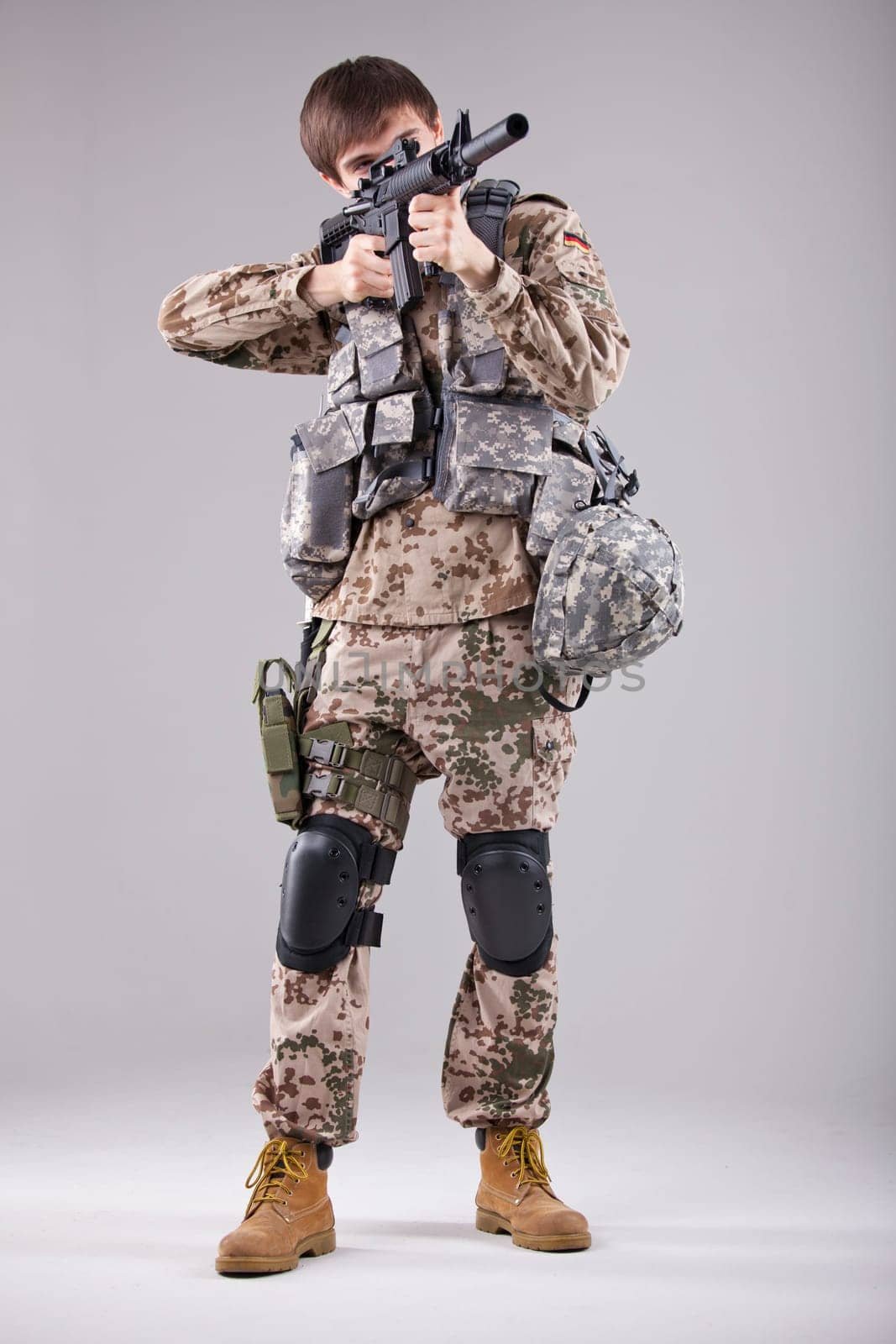 Soldier in camouflage aiming with machine gun in a white studio