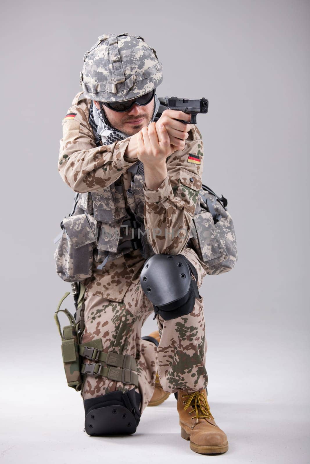 Soldier in camouflage aiming with gun in a white studio
