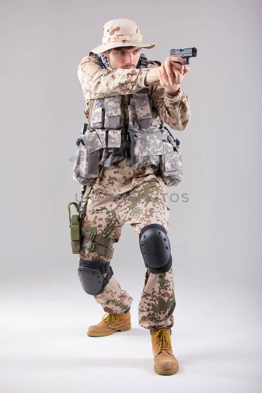 Soldier in camouflage uniform with a handgun aiming - shot in white studio