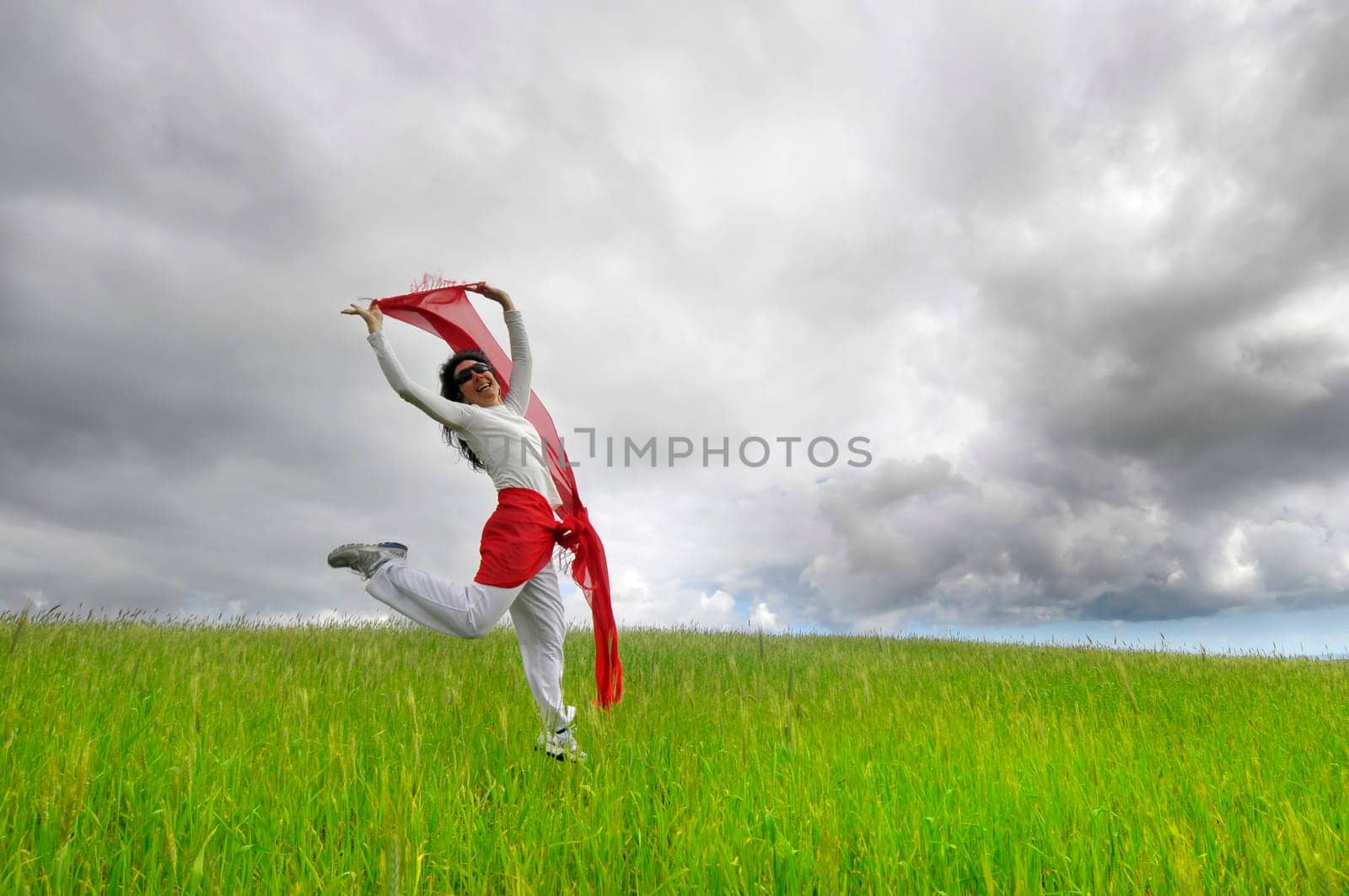 Woman jumping high in a green field with a scarf