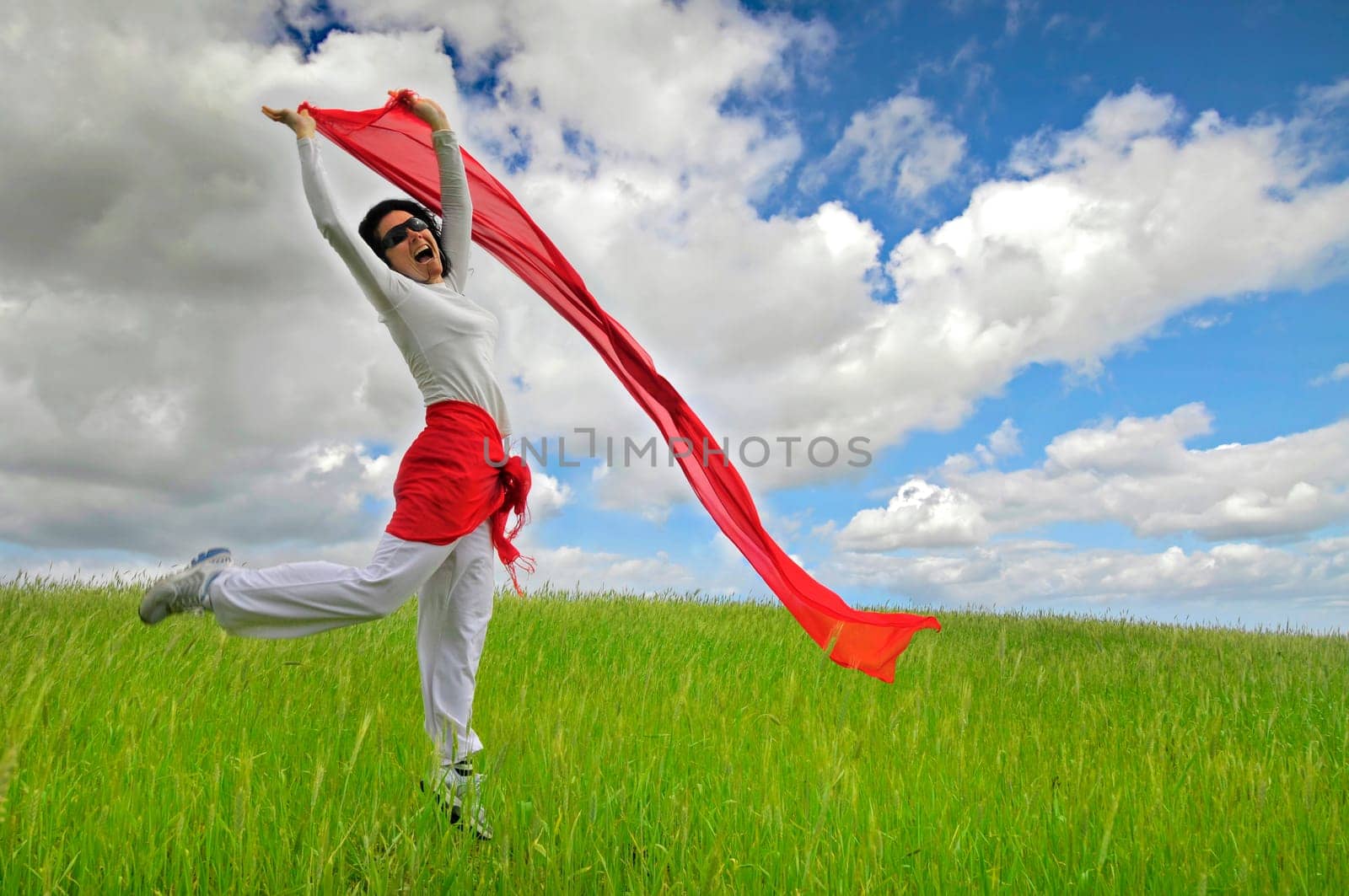 Woman jumping high in a green field with a scarf