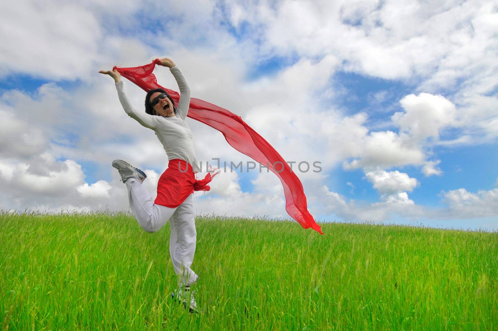 Woman jumping high in a green field with a scarf