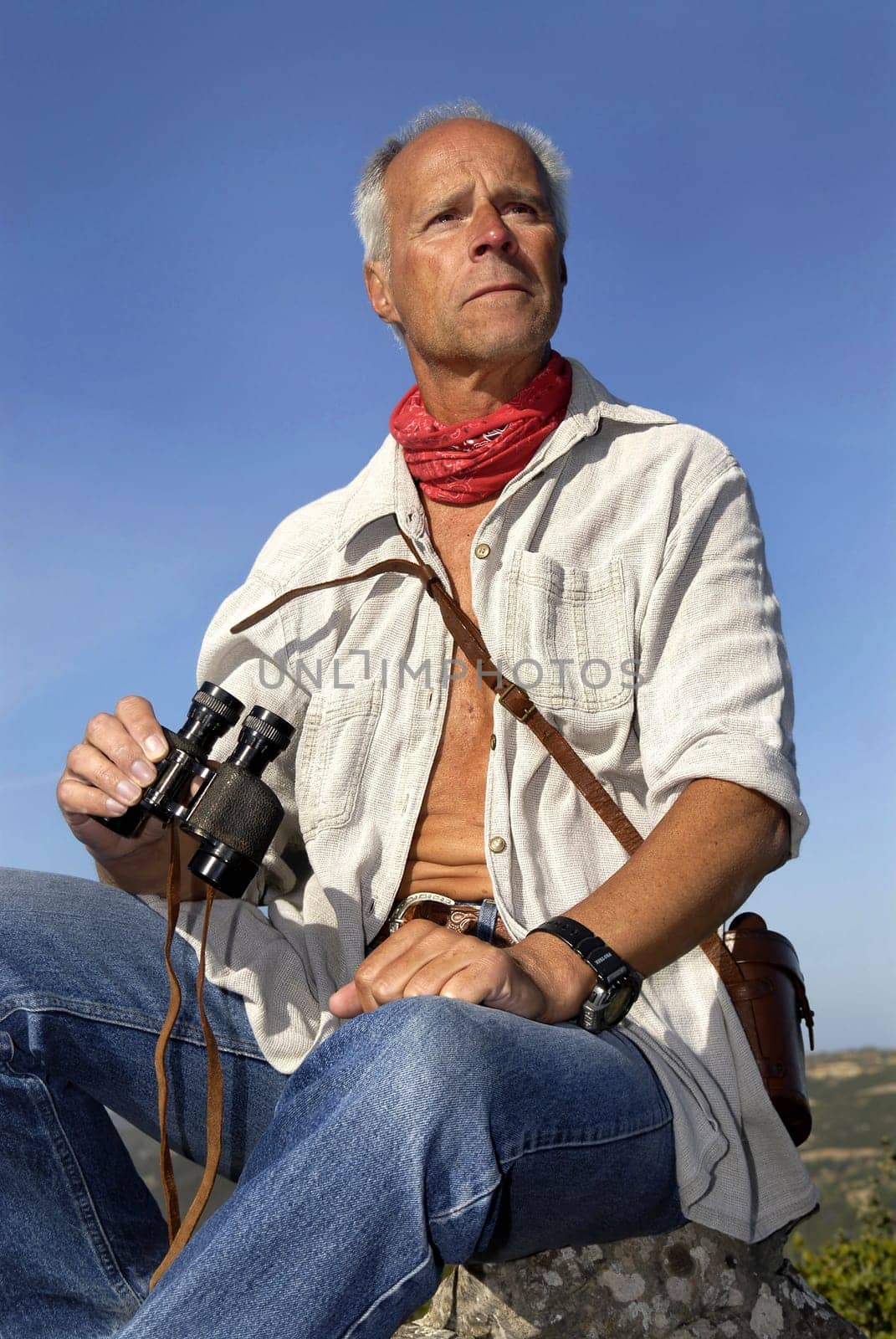 Mature man explorer looking for adventure, posing outdoors with is binoculars