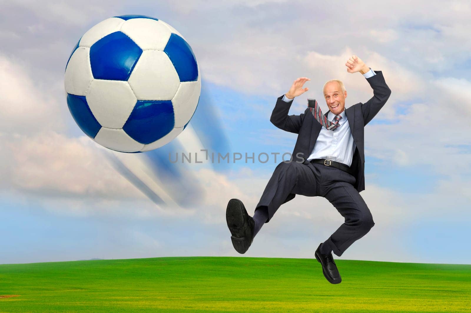 Mature businessman playing soccer outdoors in a green field