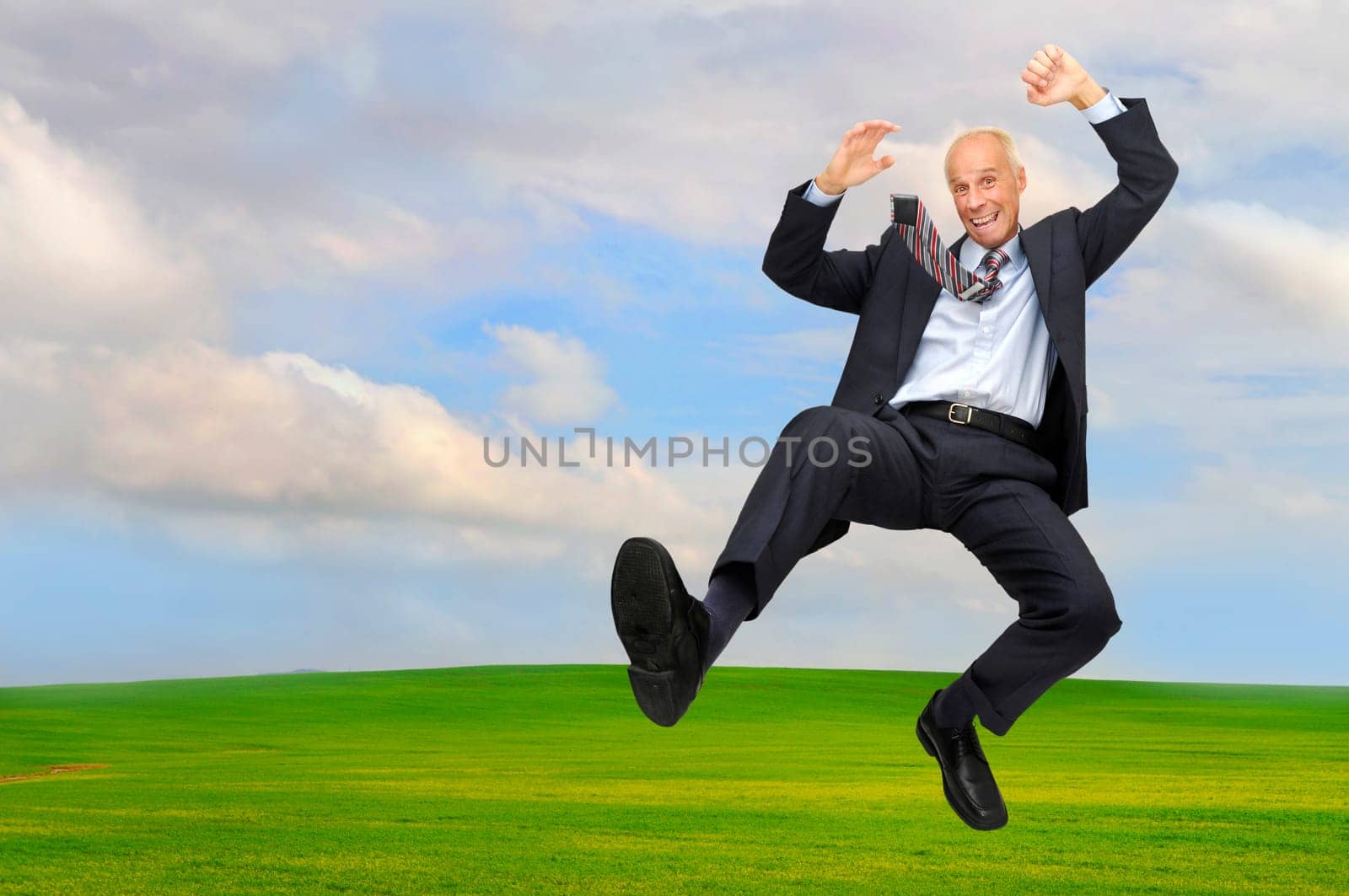 Happy mature businessman jumping outdoors in a green field