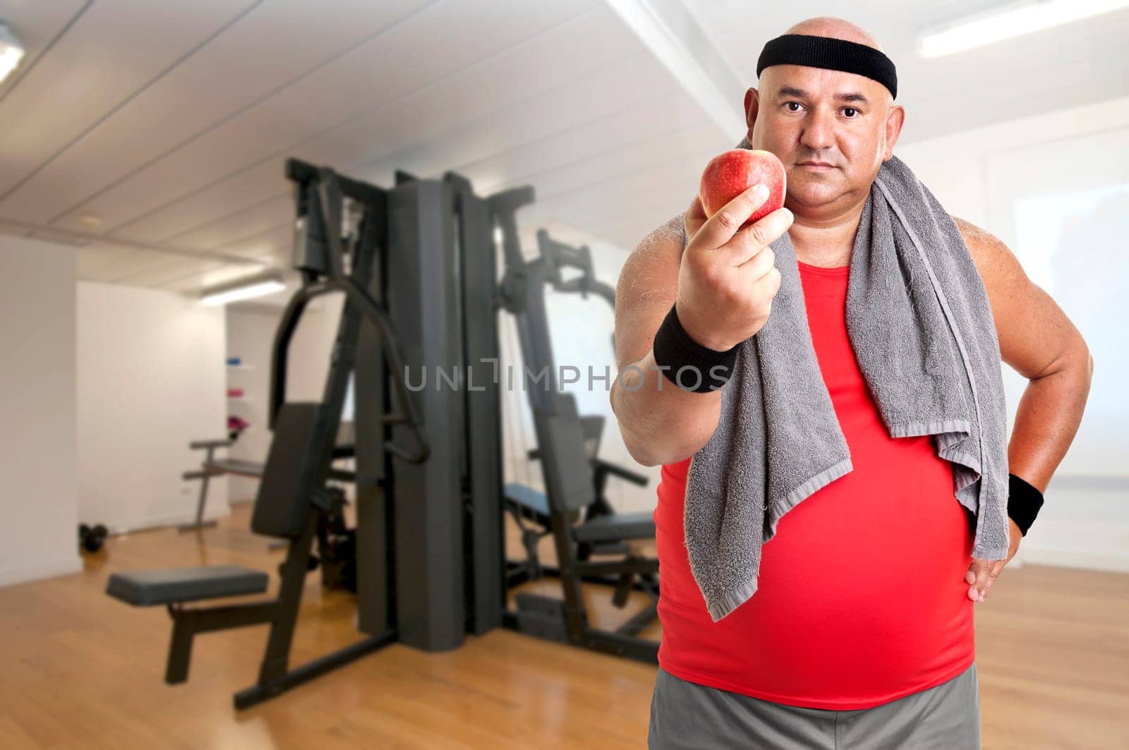 Large fitness man with an apple in the gym