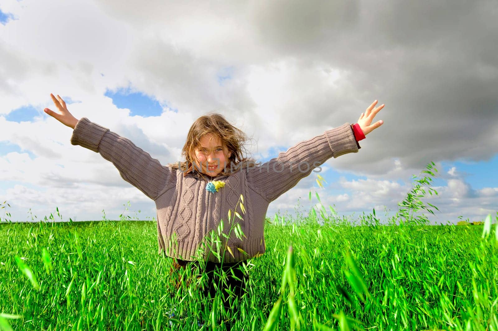 Beautiful young girl in a windy green field with open arms