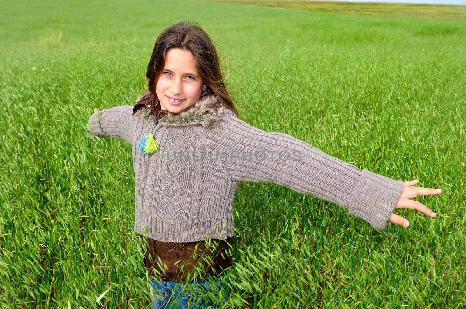 Beautiful young girl in a windy green field with open arms