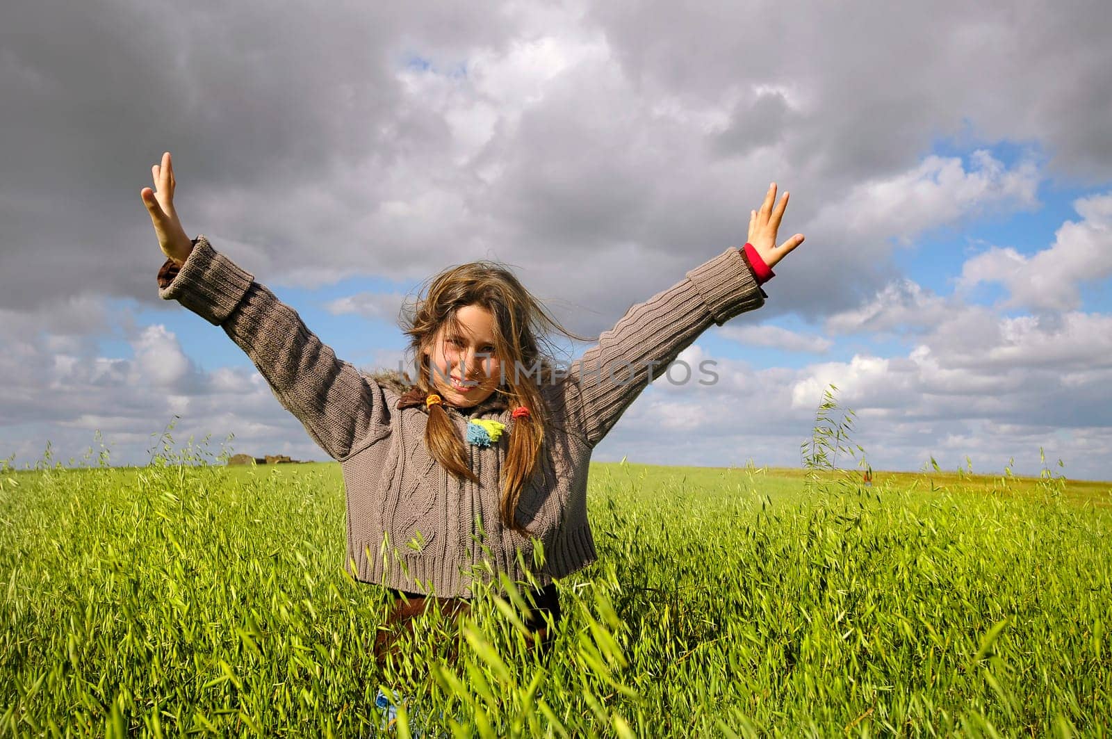 Beautiful young girl in a windy green field with open arms