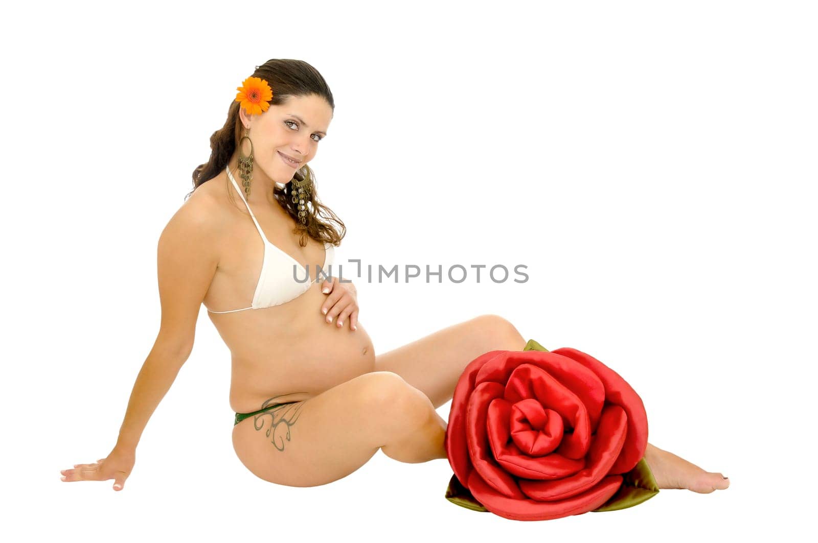 Pregnant woman with tattoo posing in bikini with a red rose isolated in white