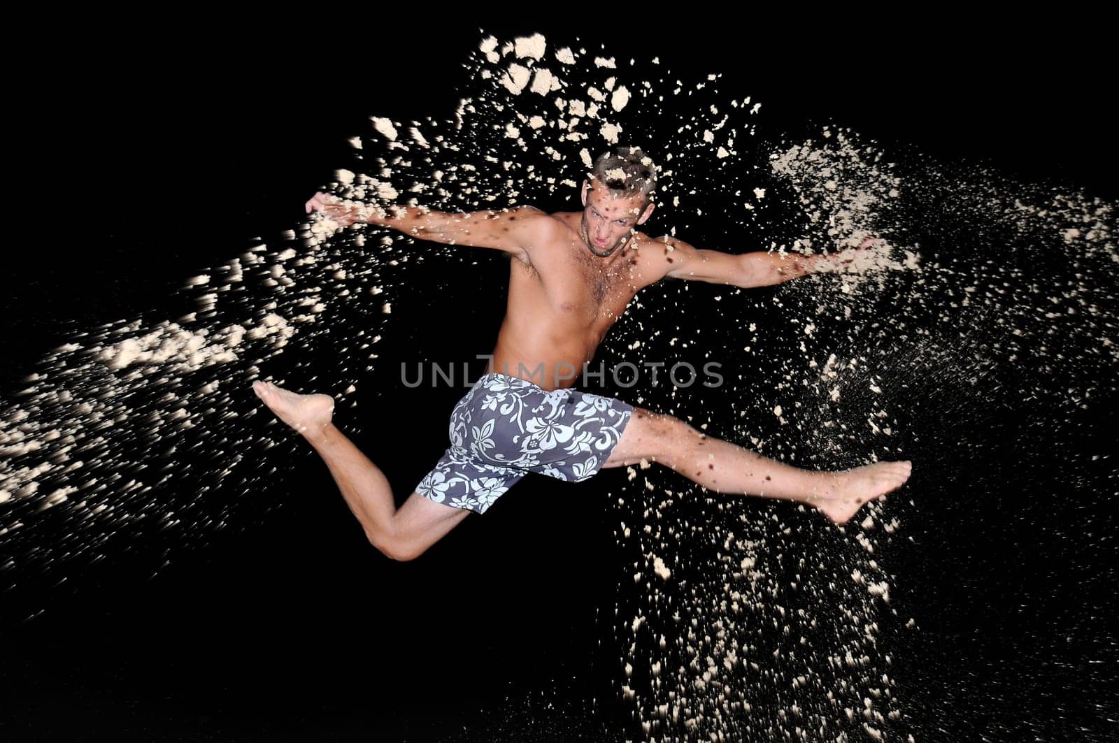 Muscular young man jumping with sand in the beach by night