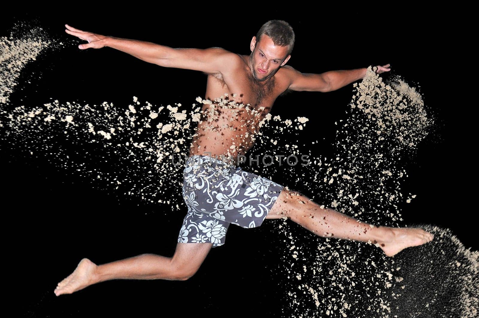 Muscular young man jumping with sand in the beach by night