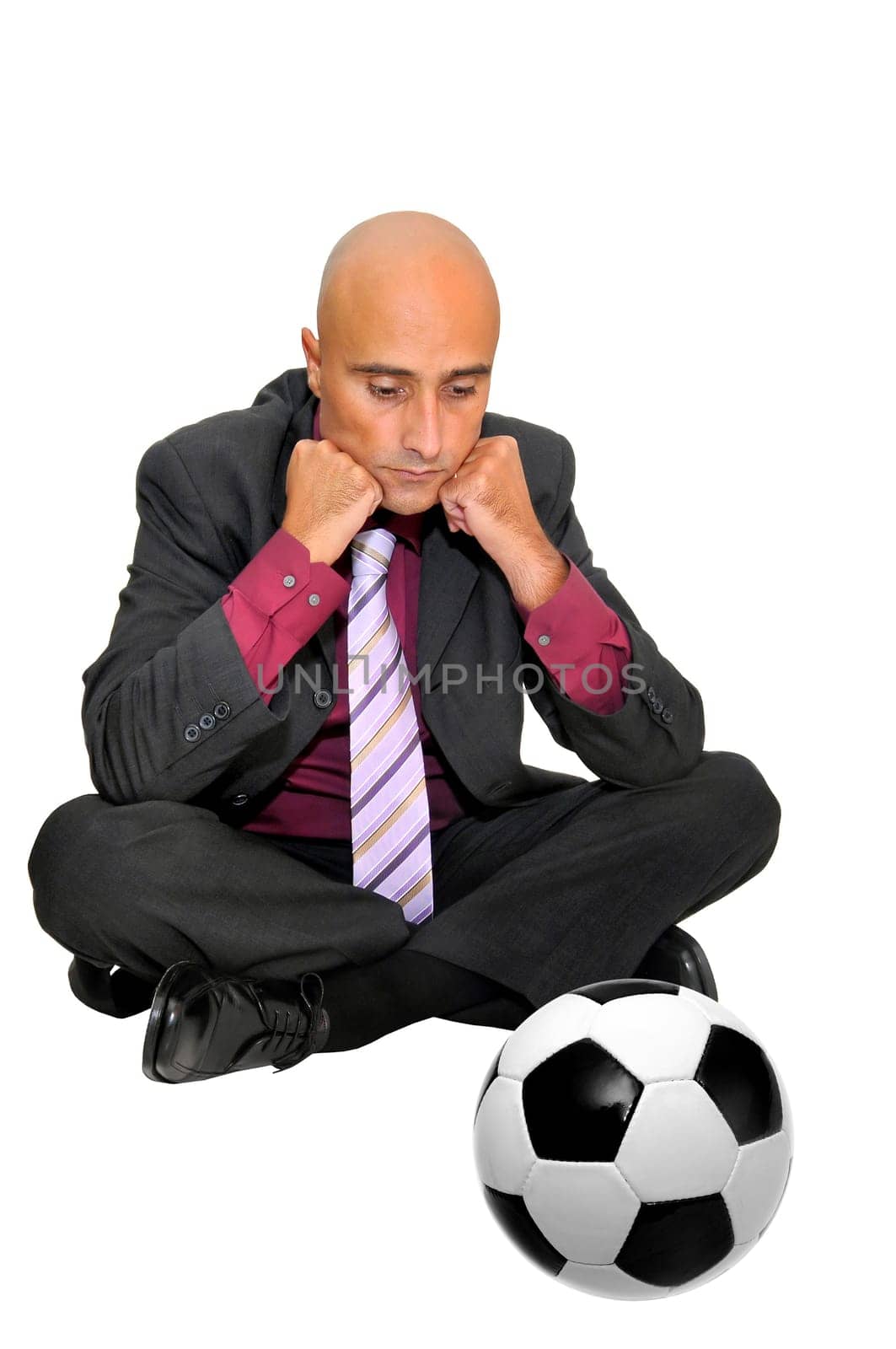 Businessman seated on the floor looking at a soccer ball, isolated in white