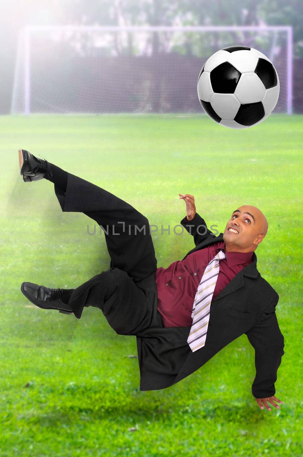 Businessman in a acrobatic pose kicking a ball in a soccer field