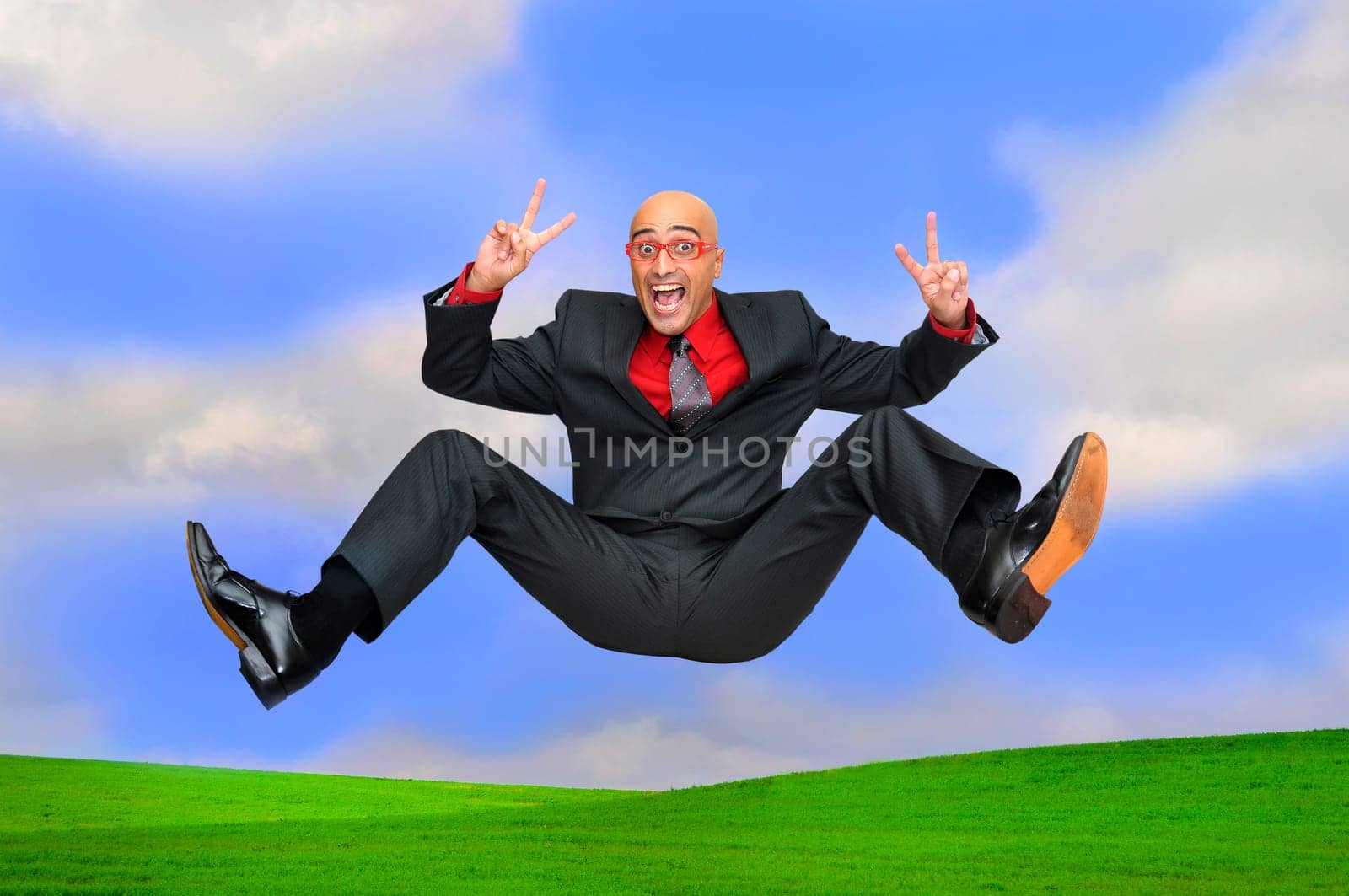 Happy businessman jumping outdoors in a green field