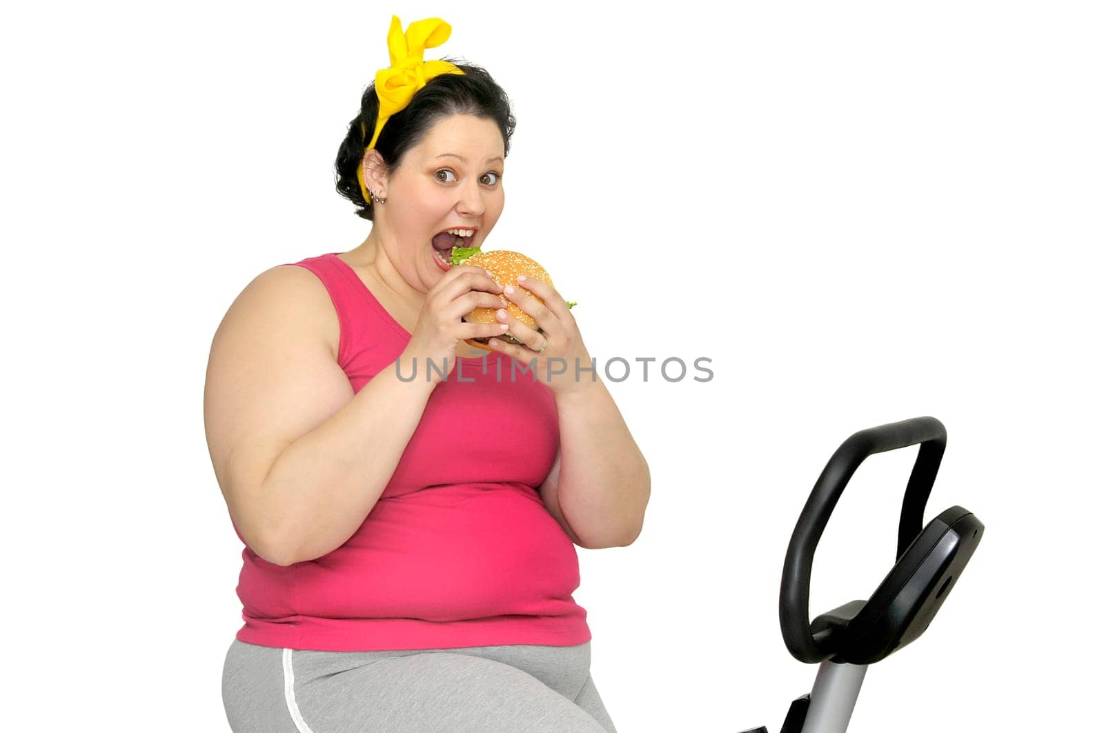 Large girl with fitness bicycle, holding a big burger isolated in white