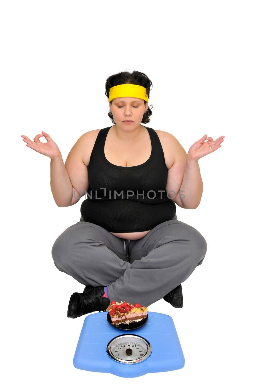 Large girl sitting near a scale with a cake trying to fight the temptation with yoga exercises