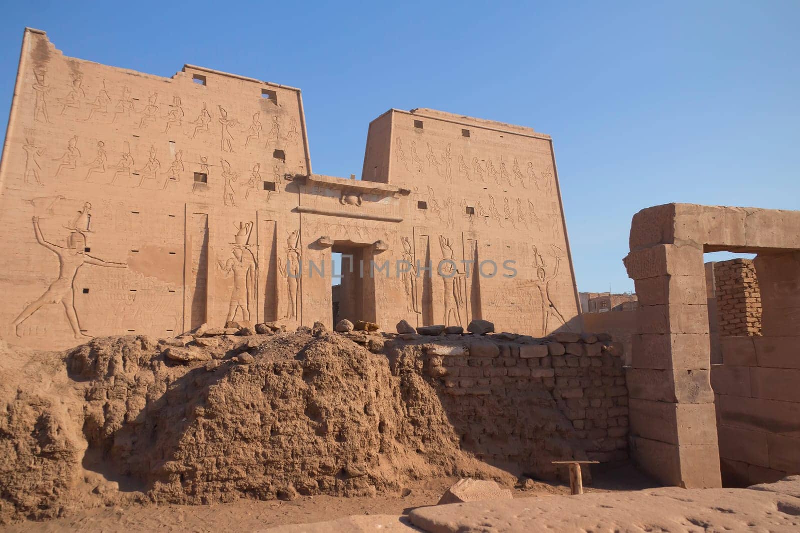 Pylon at Horus Temple with egyptian hieroglyphs. In the foreground are preserved walls that surrounded every temple in Egypt. But only in Edfu have been preserved to this day. ( Edfu, Egypt )