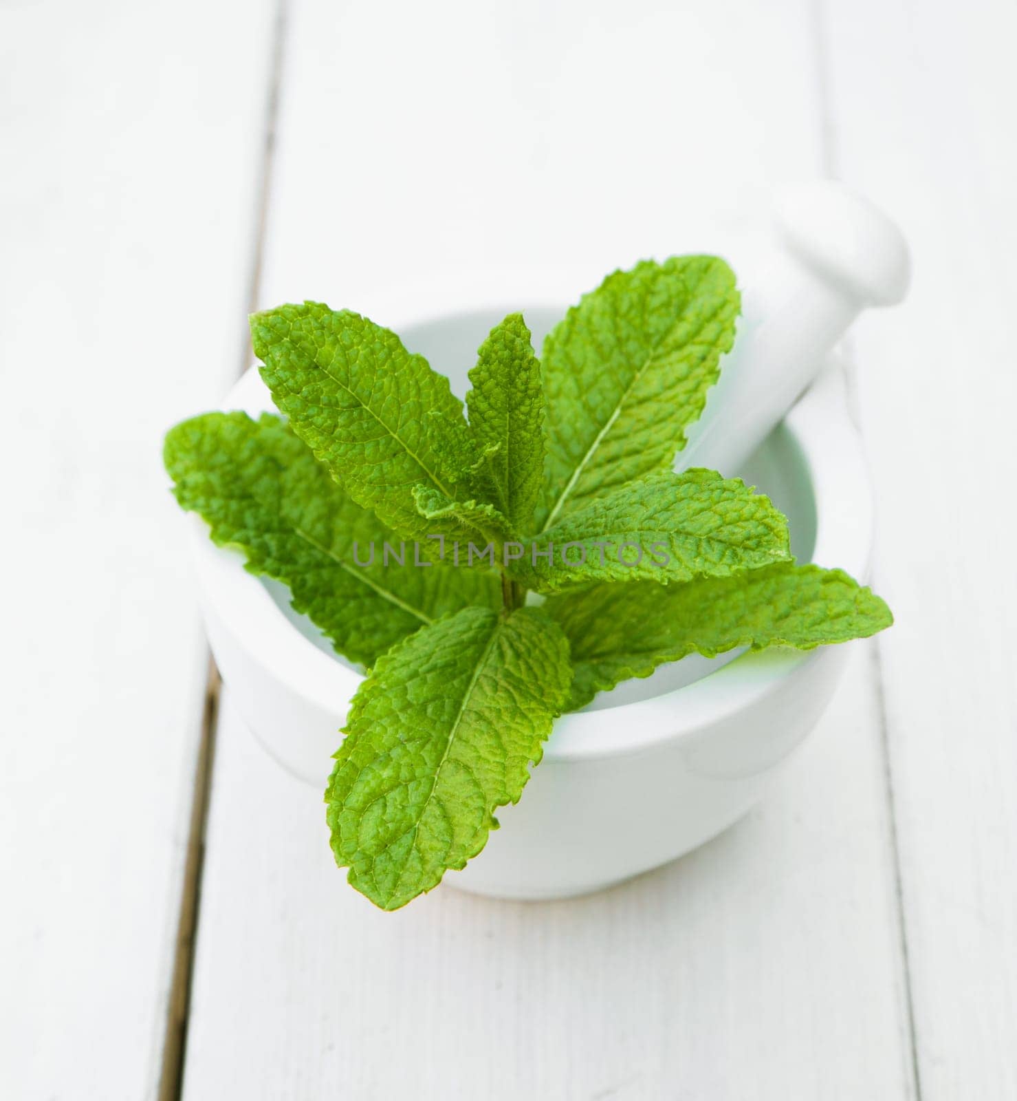 Some leaves of Mint in a mortar with pestle on a wooden table for herbs concepts