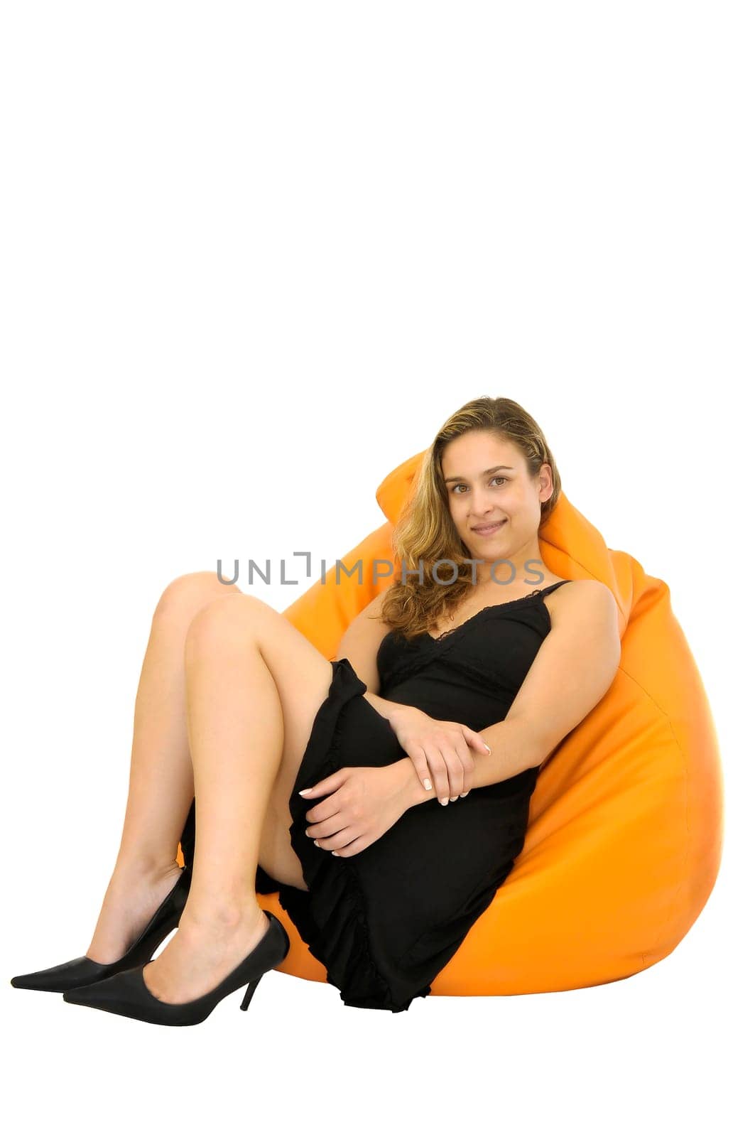 Beautiful young woman posing with a black dress seated in a yellow puff isolated in white