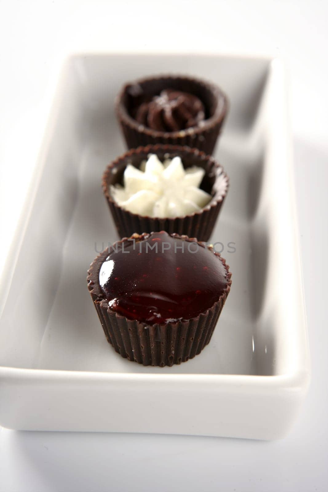Three little chocolate cakes in a line with cream and strawberry  jam