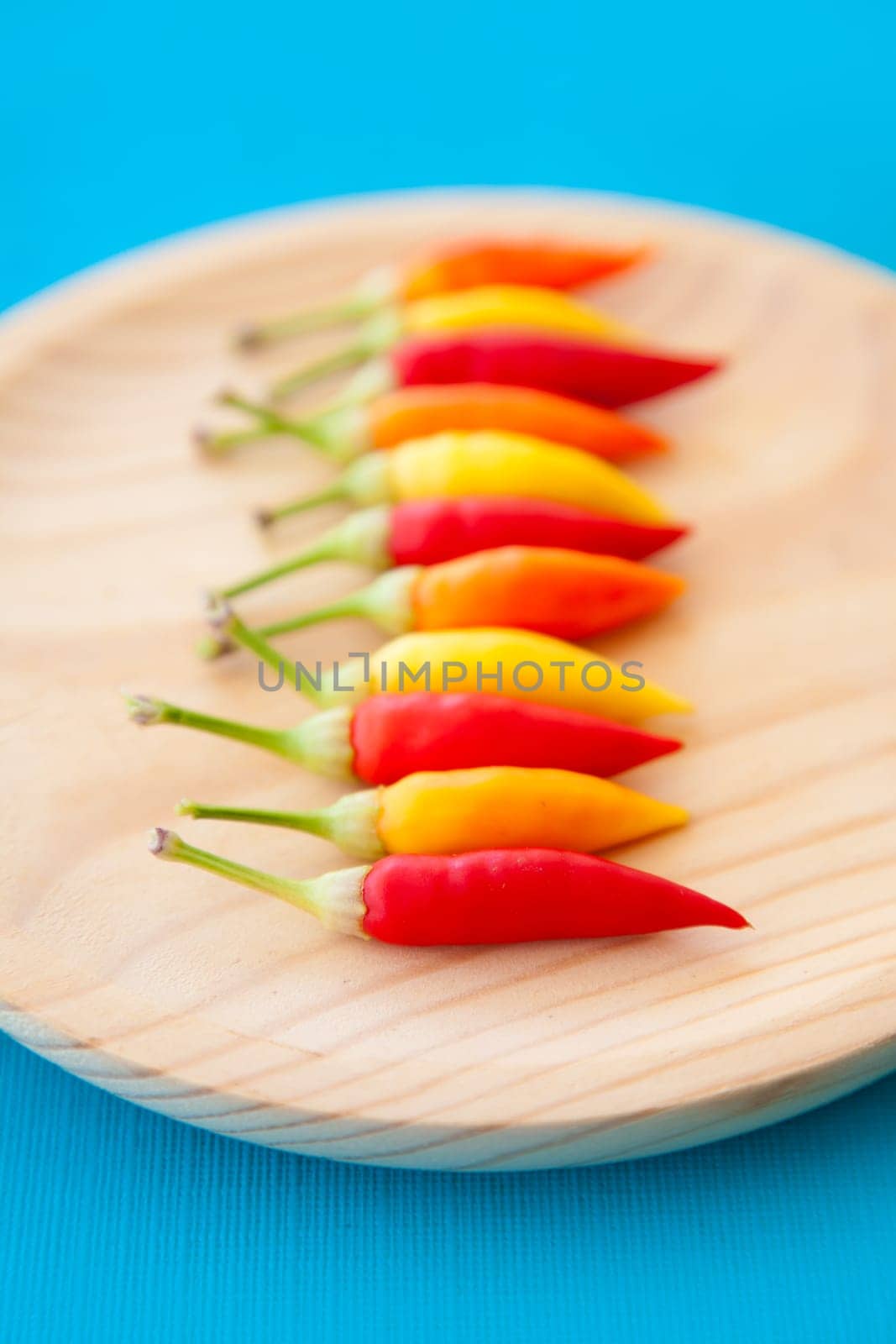 colorful hot chili peppers in a row on wooden plate
