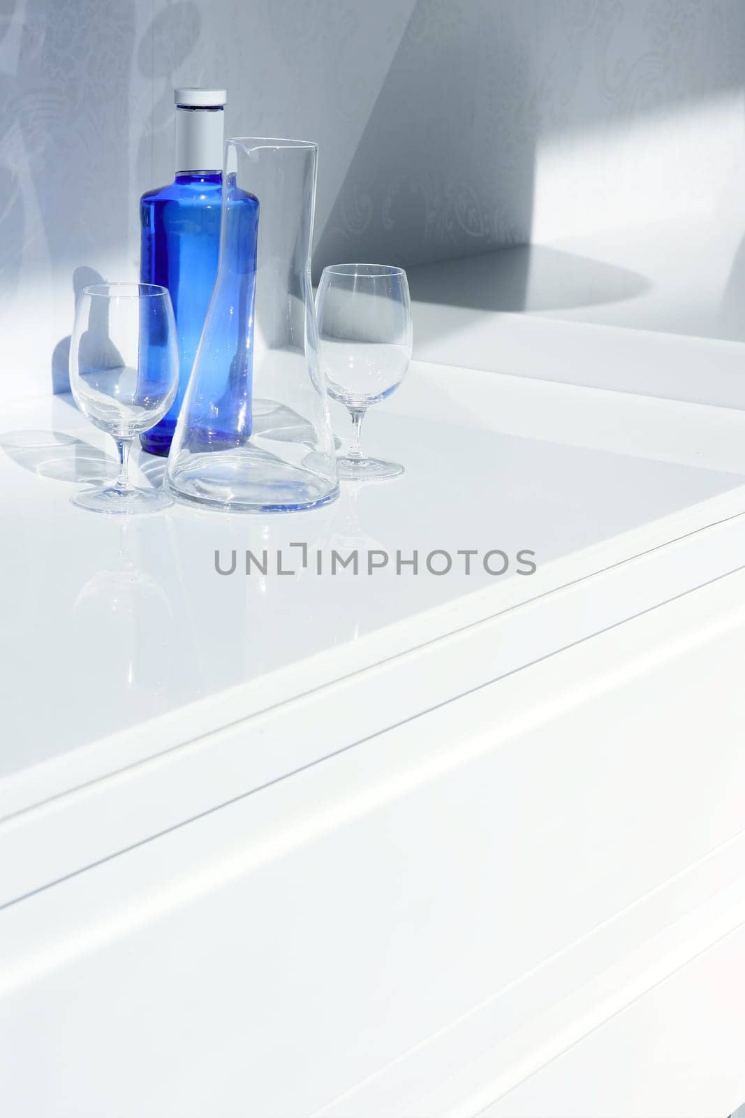 Blue water bottle with glass, transparent shadow in white kitchen