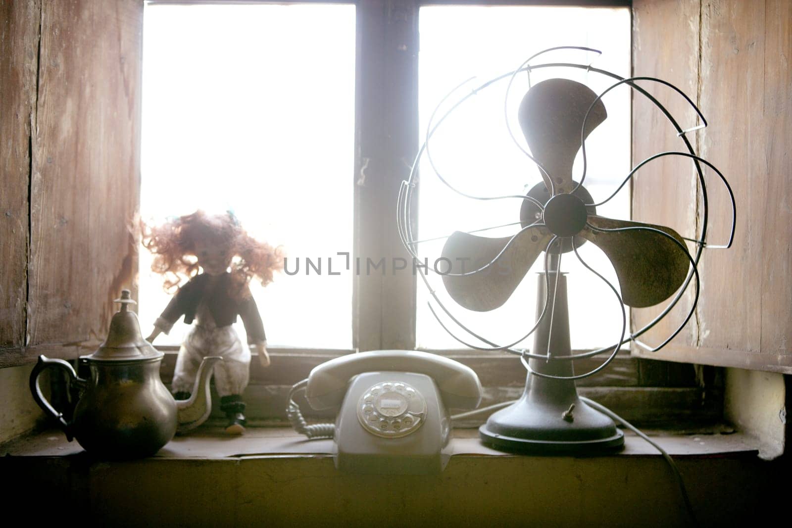 Antique vintage air fan, doll and phone at the window backlight