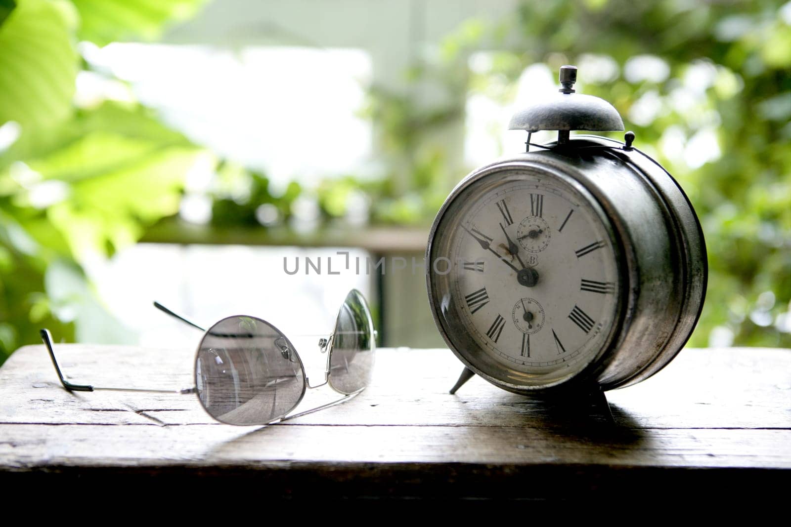 Old alarm bell clock at the window backlit in a house room with plants
