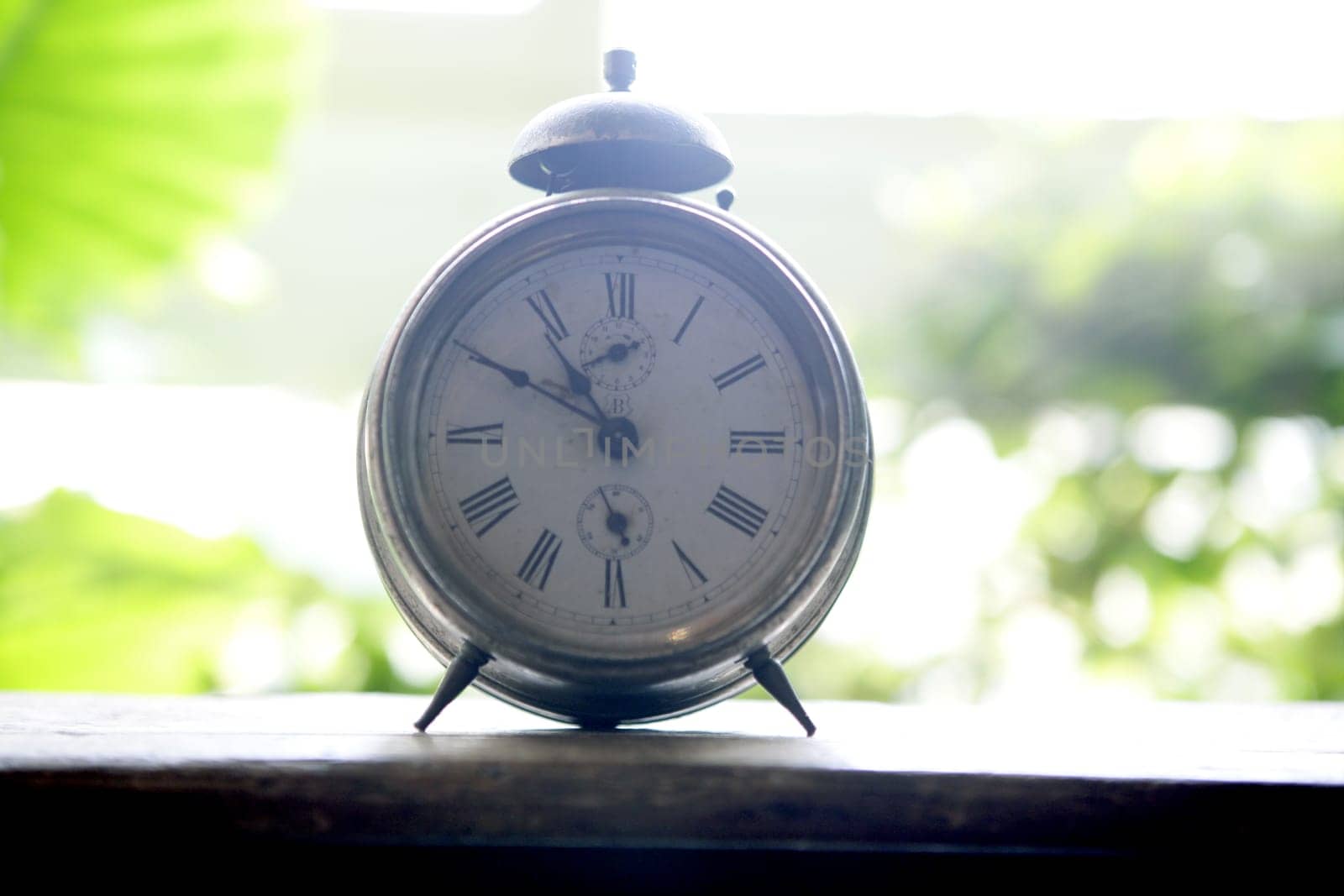 Old alarm bell clock at the window backlit in a house room with plants
