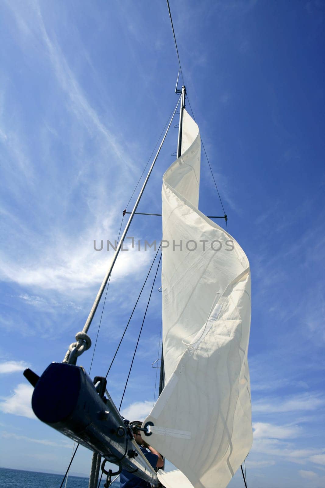 Sailor in sailboat rigging the sails over sunny summer blue sky