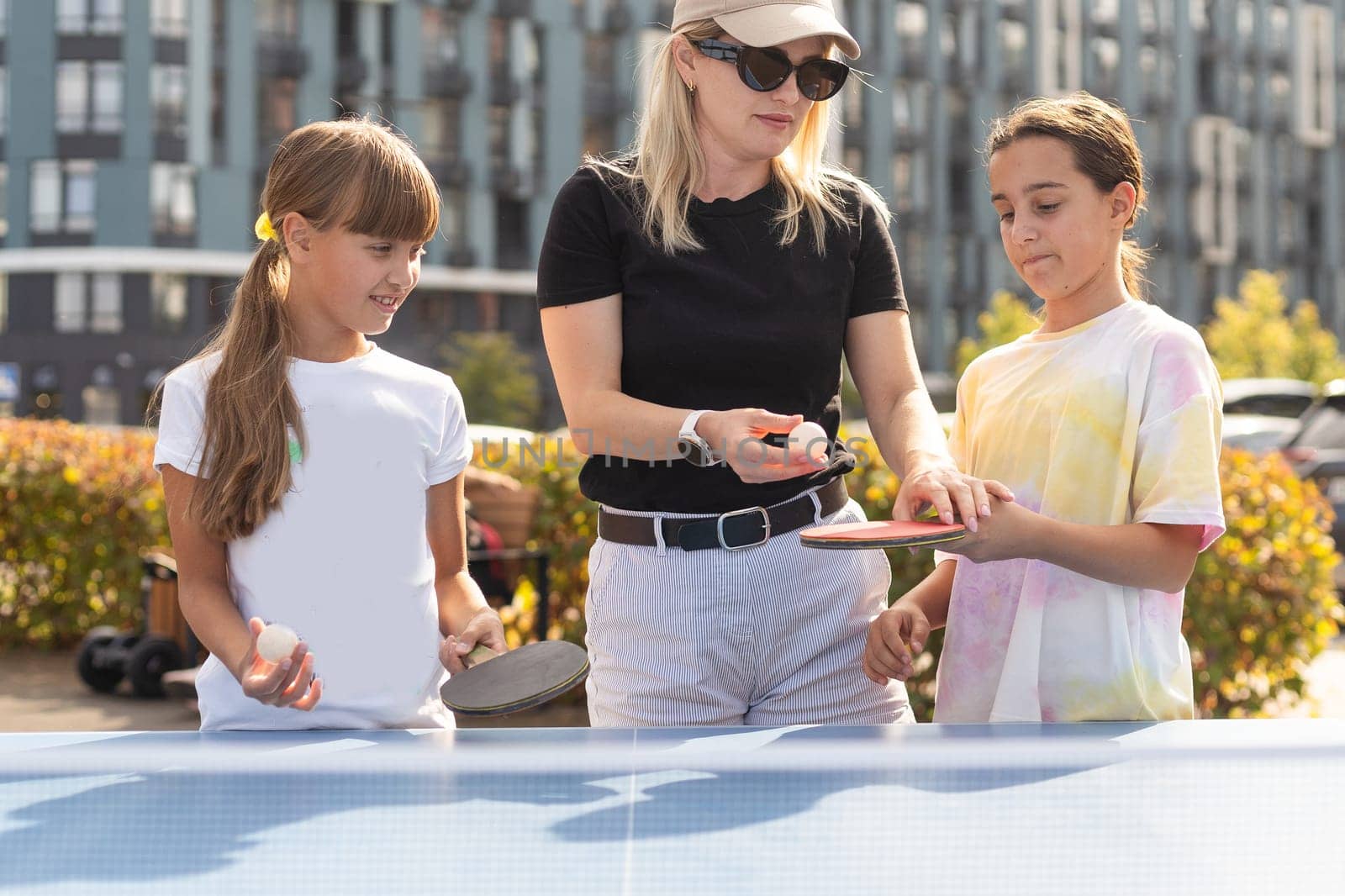Young woman with her daughters playing ping pong in park. High quality photo