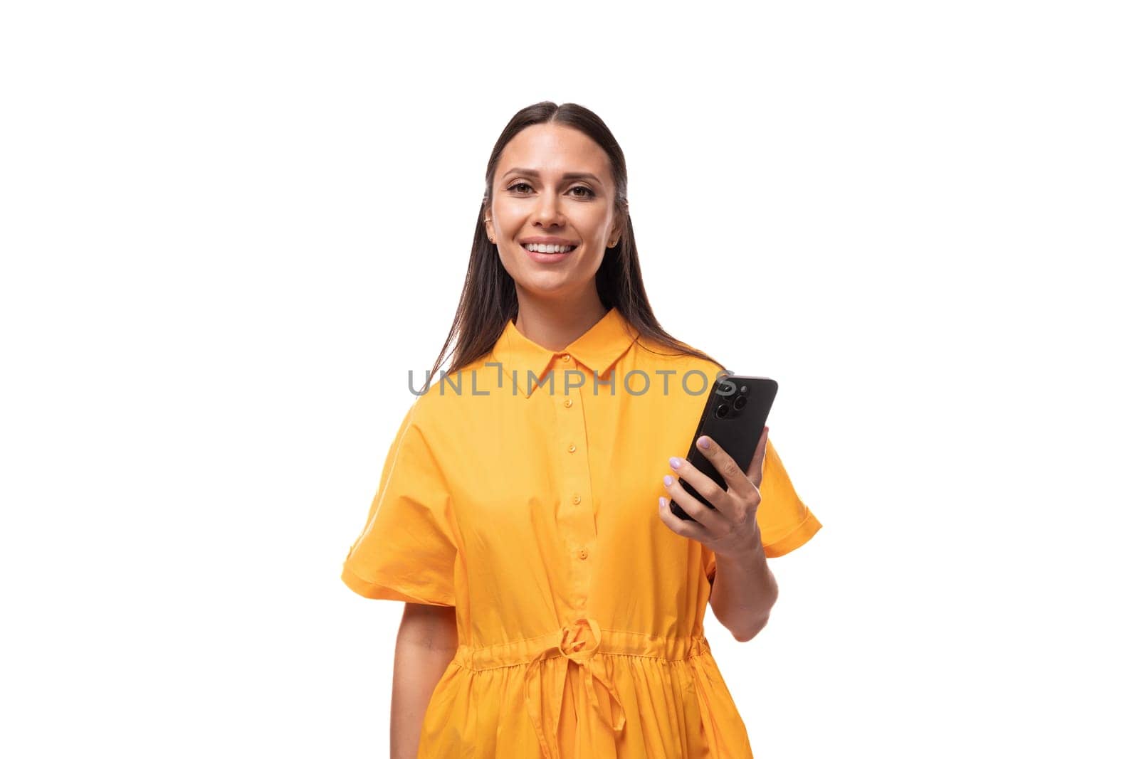 european young woman with black hair dressed in an orange summer dress on vacation holding a smartphone.