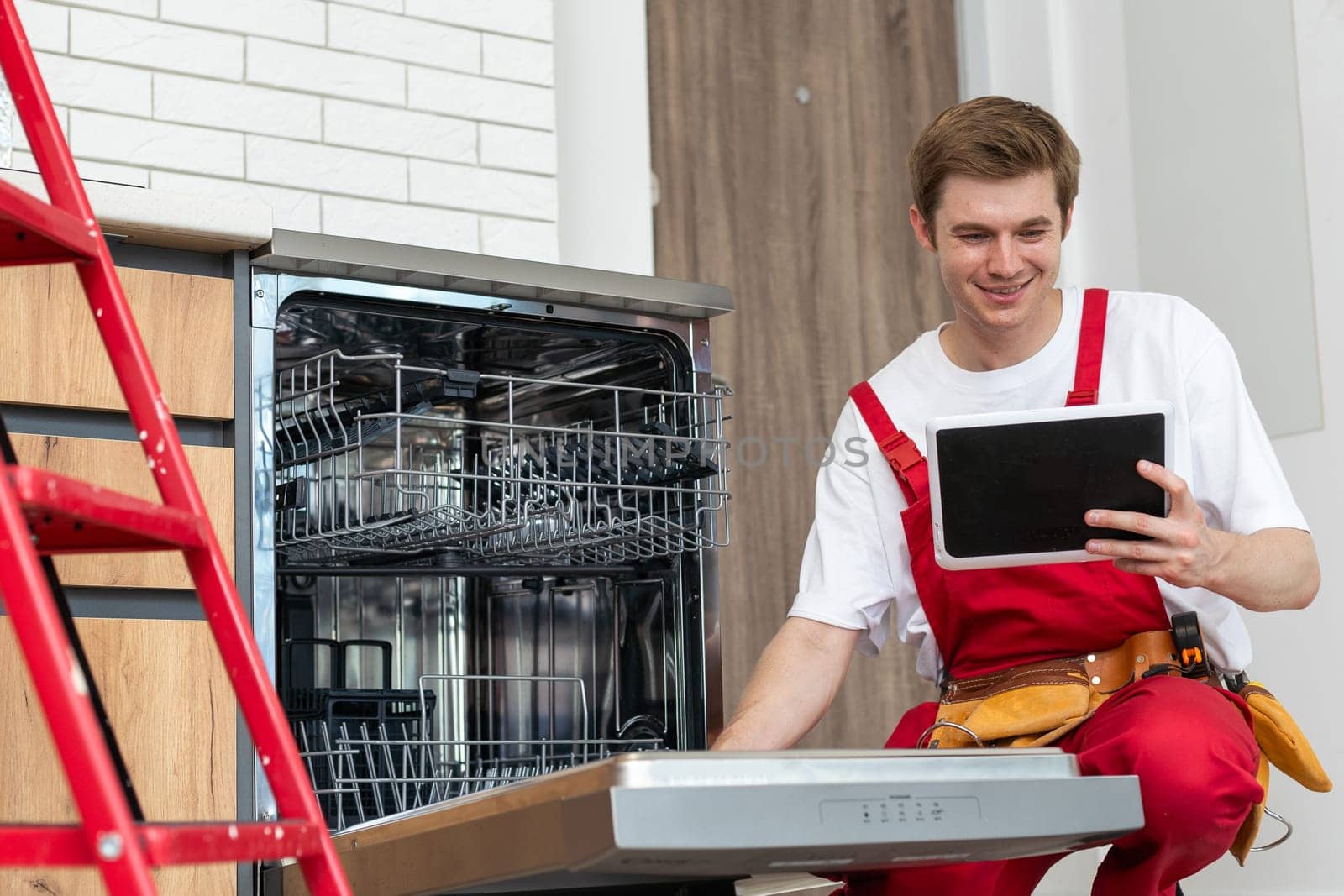 Portrait Of Male Technician Repairing Dishwasher In Kitchen using digital tablet