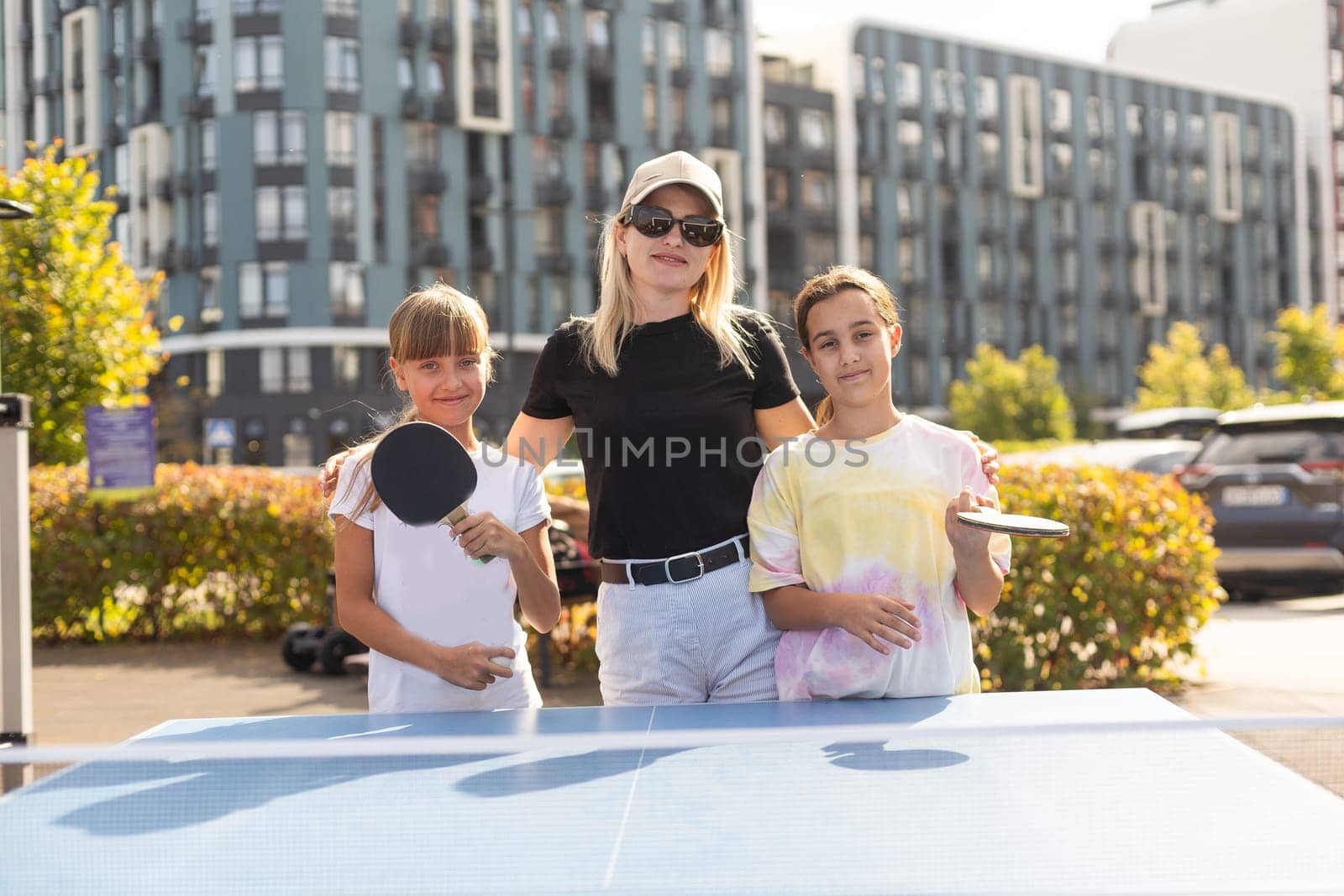 Young woman with her daughters playing ping pong in park. High quality photo