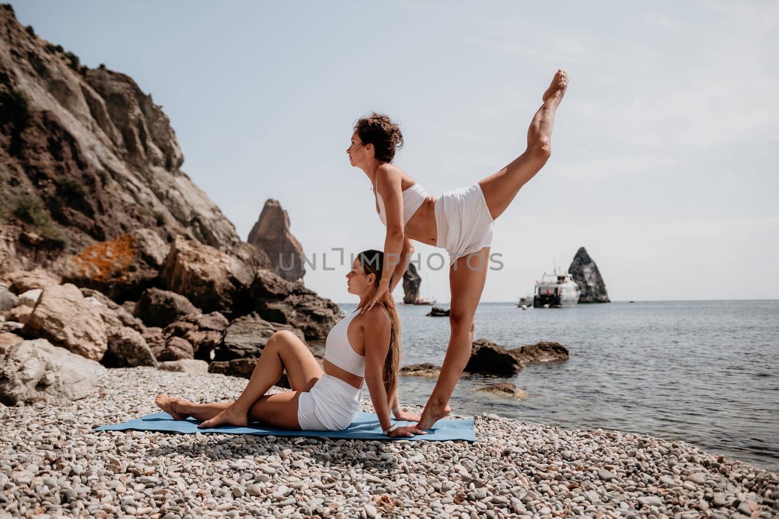 Woman sea yoga. Two Happy women meditating in yoga pose on the beach, ocean and rock mountains. Motivation and inspirational fit and exercising. Healthy lifestyle outdoors in nature, fitness concept. by panophotograph