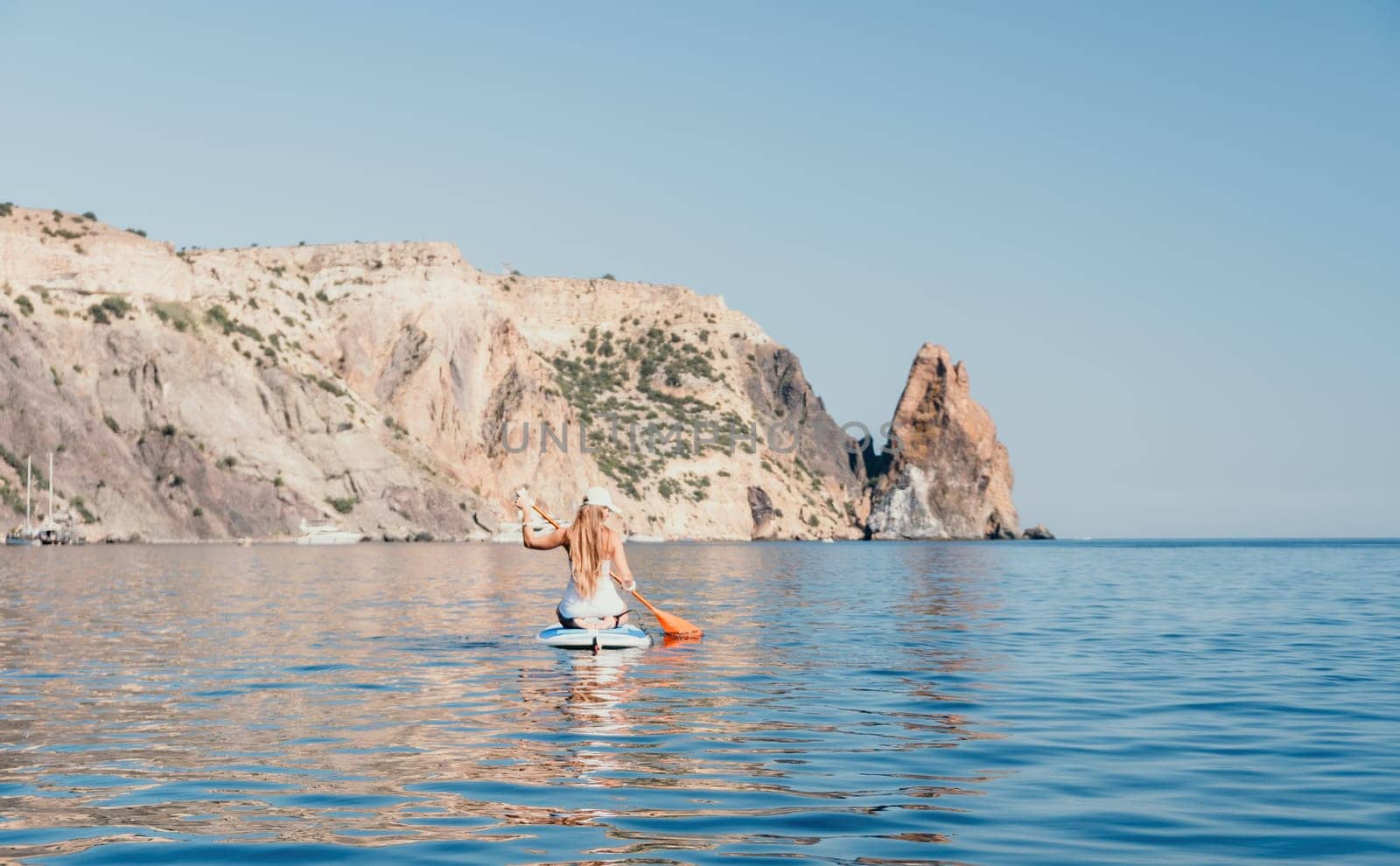 Close up shot of beautiful young caucasian woman with black hair and freckles looking at camera and smiling. Cute woman portrait in a pink bikini posing on a volcanic rock high above the sea