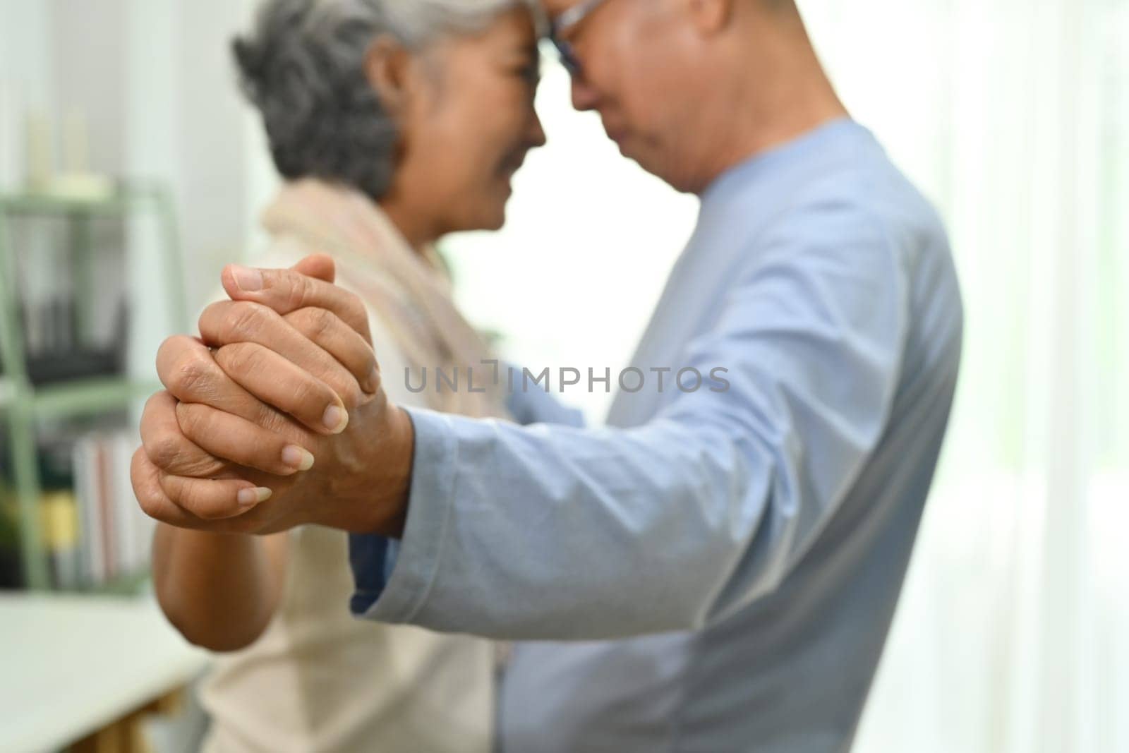 Romantic elderly couple spouses dancing in living room and looks at each other with love.