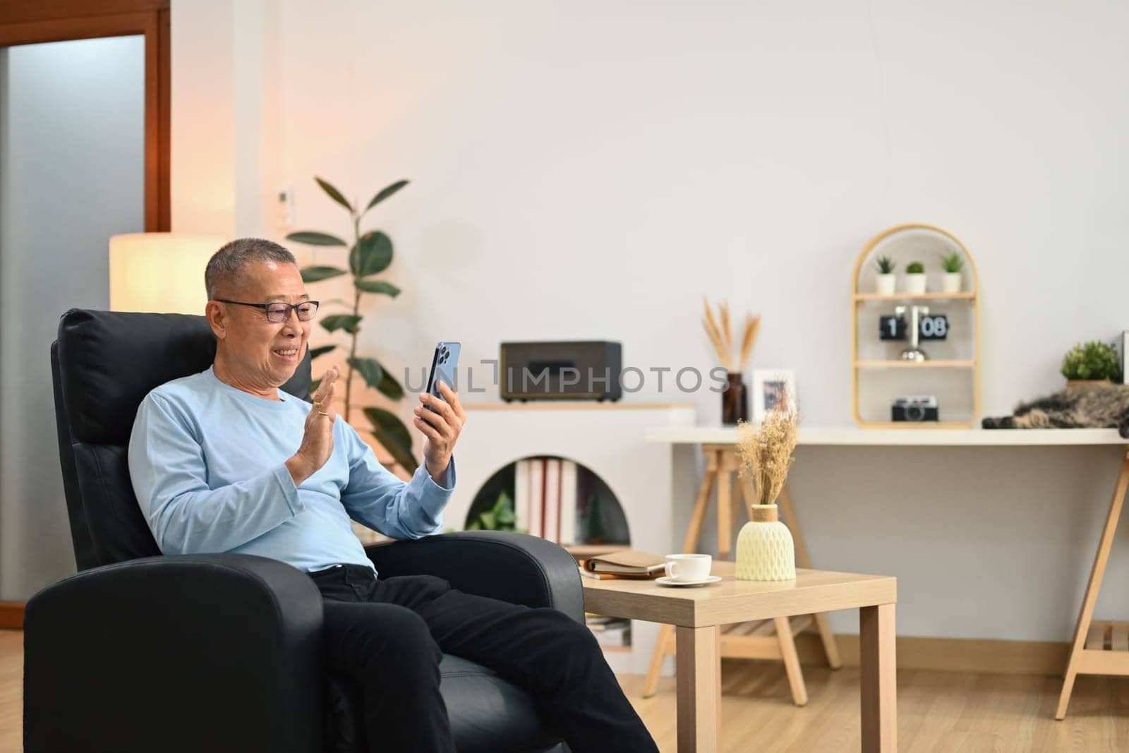 Happy elderly man waving hand while talking online on smartphone with family.