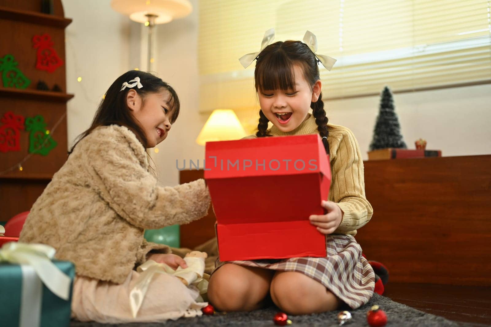 Surprised cute little children opening Christmas present in decorated living room by prathanchorruangsak