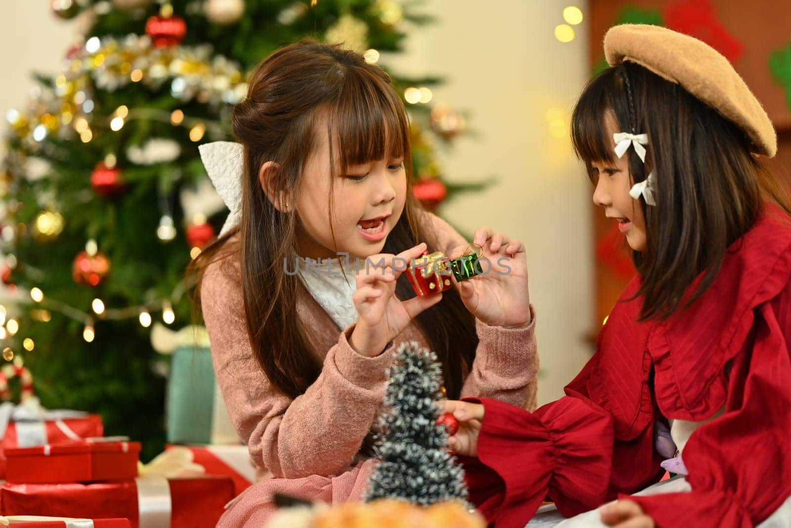 Two little children wearing warm winter clothes decorating small Christmas tree in living room by prathanchorruangsak