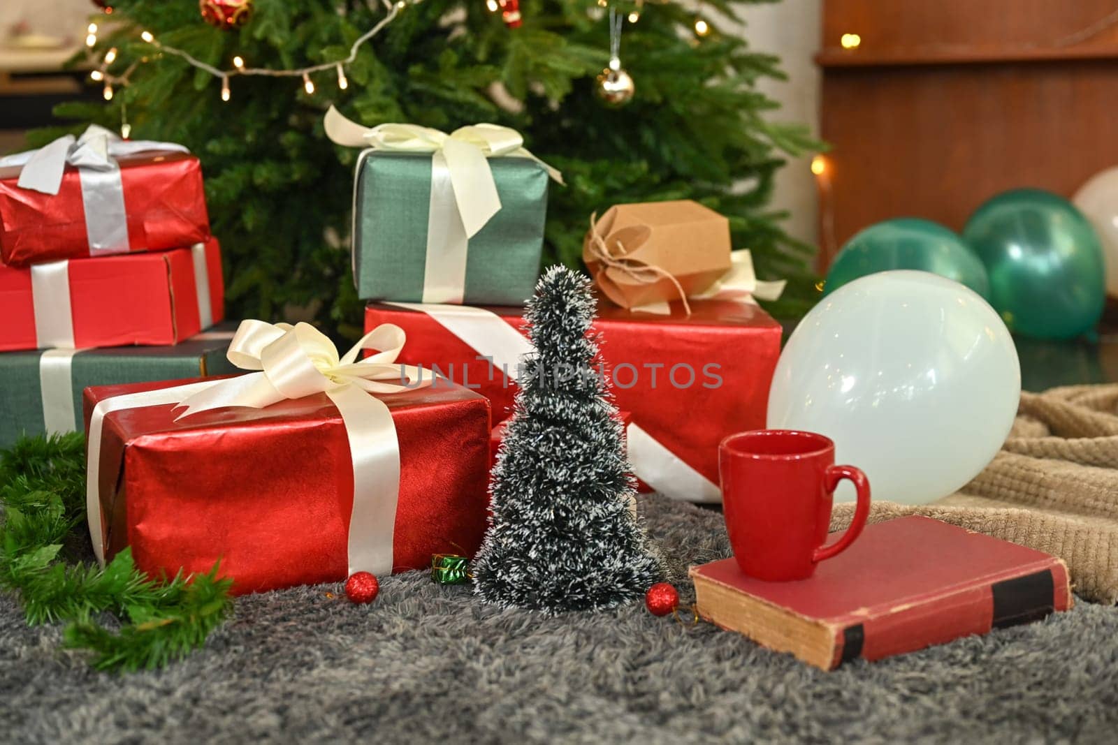 Pile of gift boxes, coffee cup and book on floor near decorated Christmas tree. Winter holiday celebration concept by prathanchorruangsak