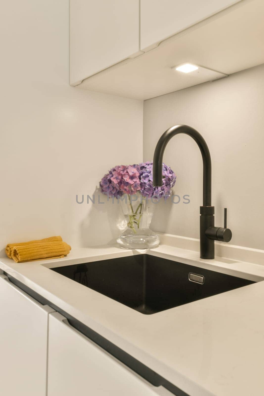 a kitchen sink with flowers in a glass vase on the countertop and black fauced fae over it