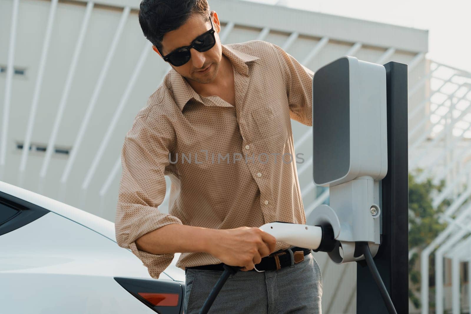 Young man put EV charger to recharge electric car battery. Expedient by biancoblue