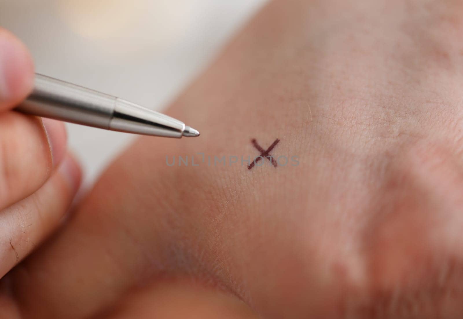 Male make x cross note with silver pen at his arm for keep in mind in office closeup. Try not to forget to do list concept
