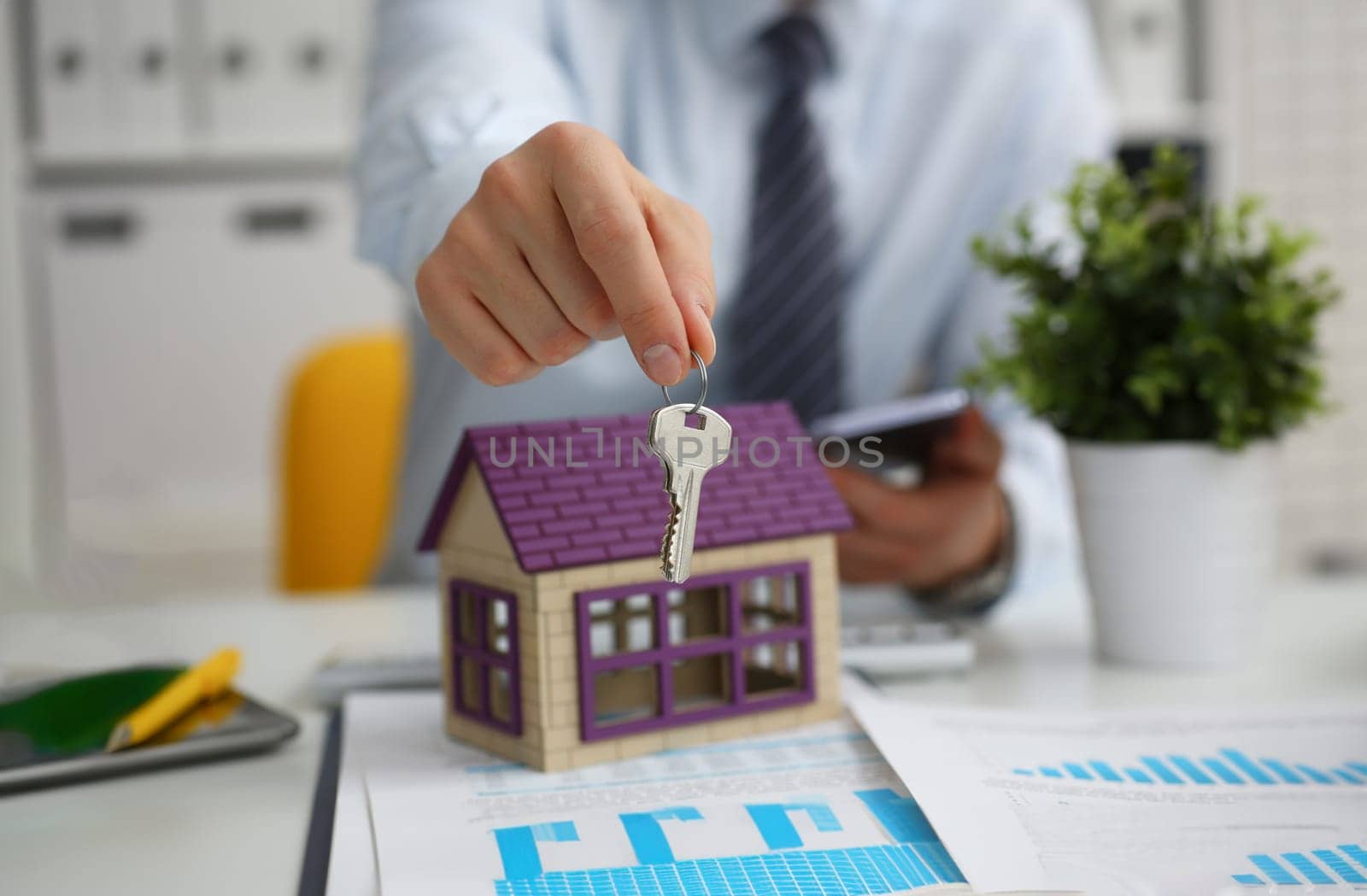Male hand holds the key to the lock in the hand against the backdrop of the toy house. Sale purchase lease concept real estate services on the market.